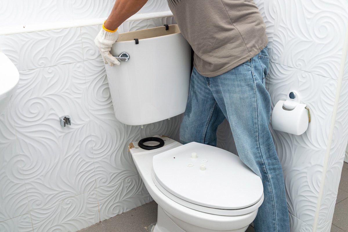 A person reinstalling a toilet tank after replacing the toilet flush valve.