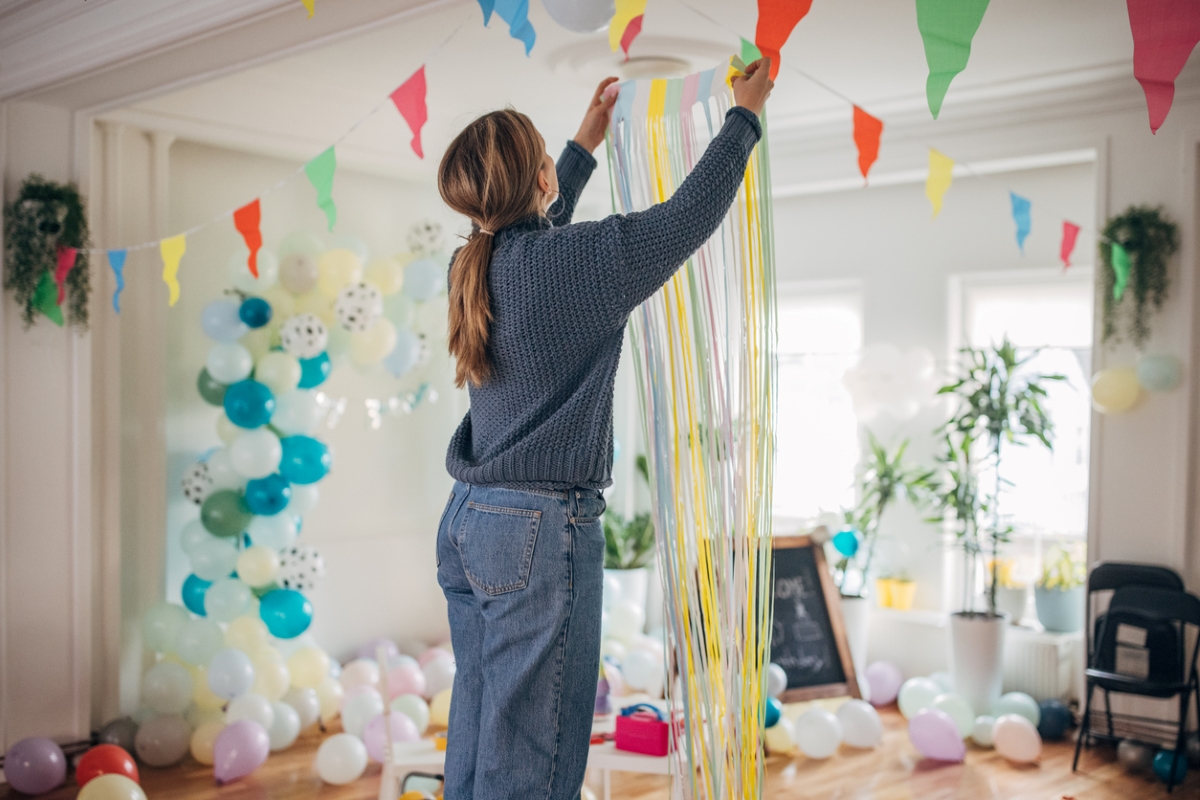 Woman hanging paper curtain in room with balloons.