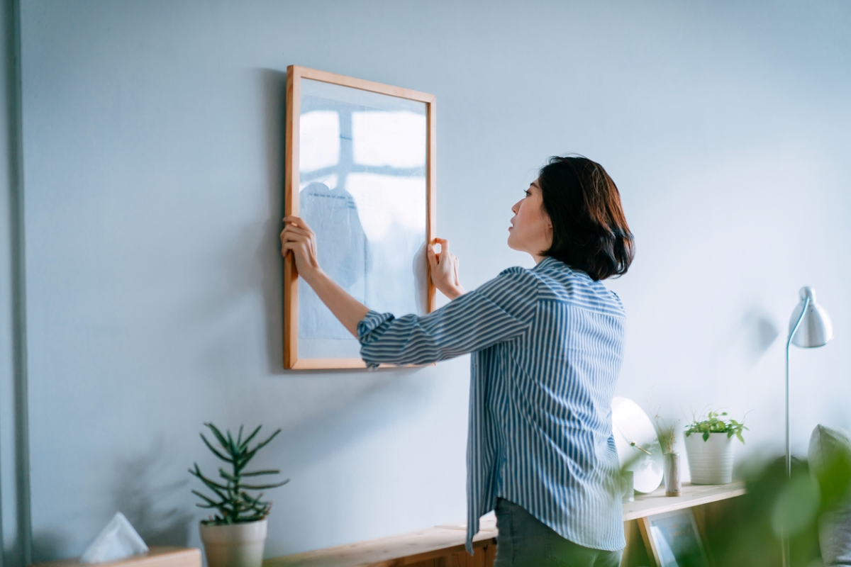 Woman hanging large picture frame on blue wall.