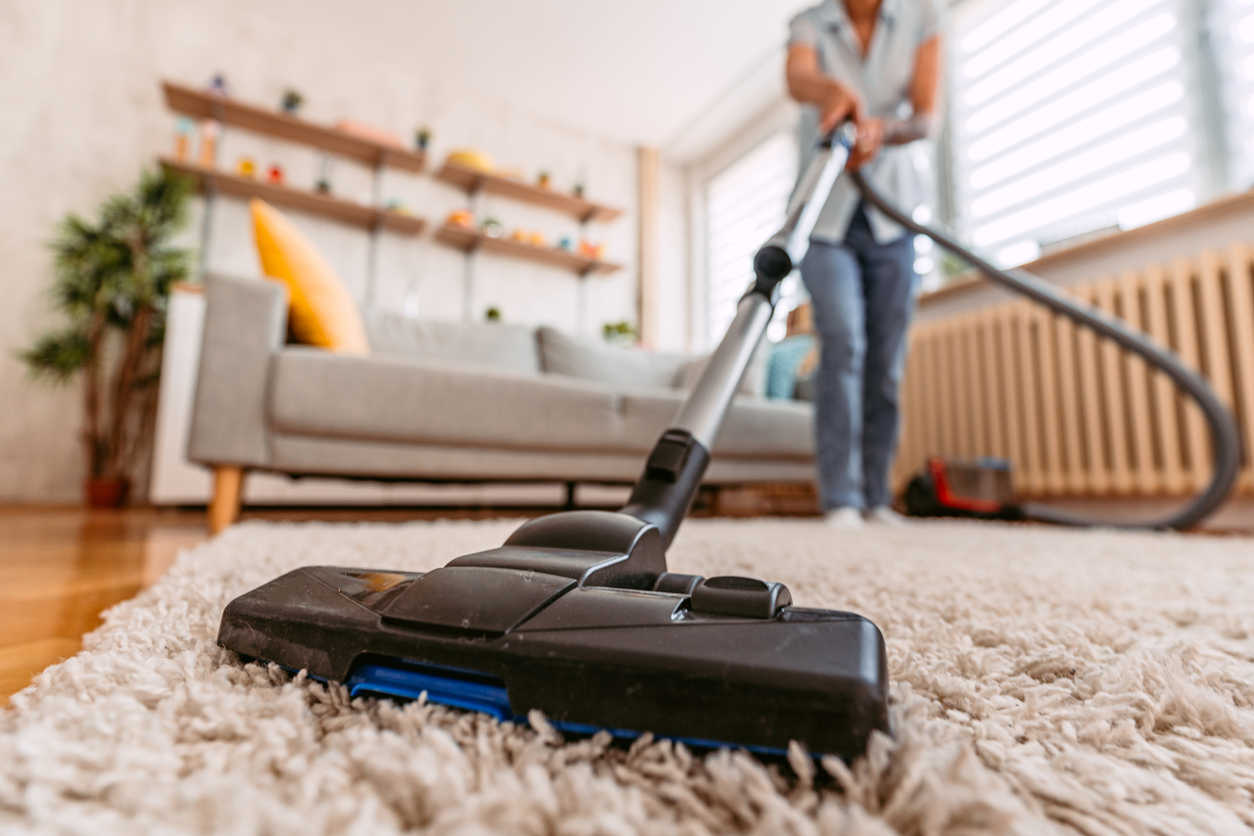 Woman in jeans uses vacuum cleaner to clean beige rug.