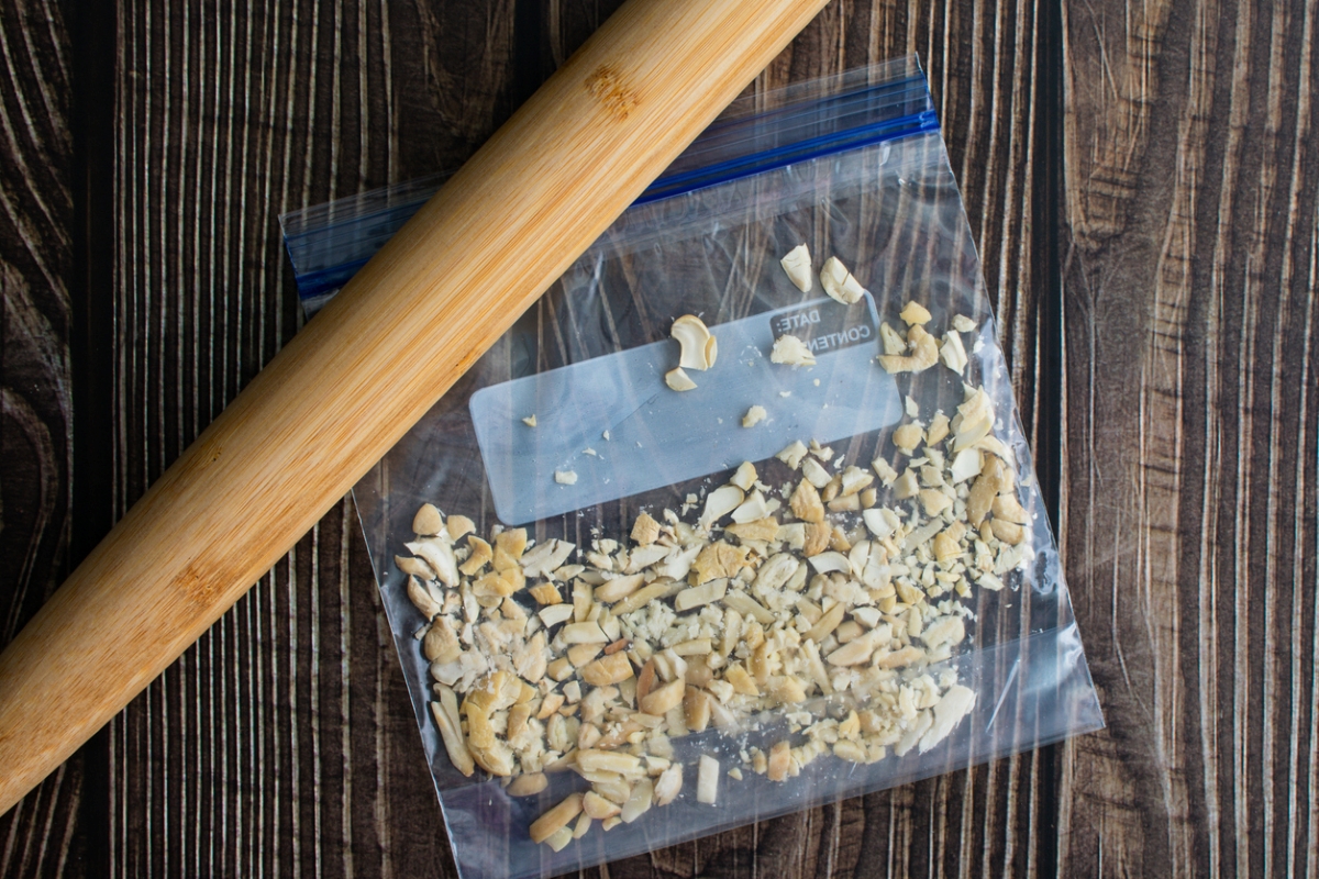 Nuts in plastic bag crushed by wooden rolling pin.