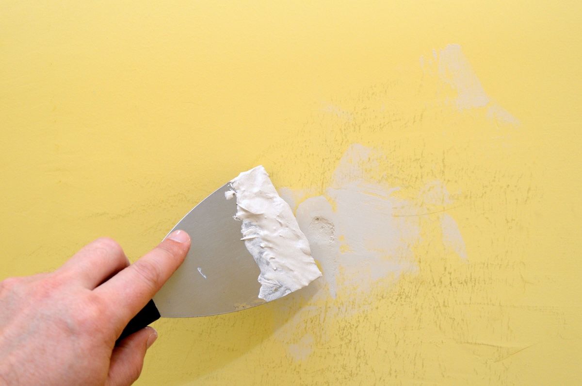 A person repairing walls with drywall spackle.