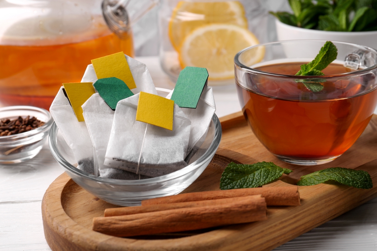 Tea bags in a clear bowl next to cup of tea.