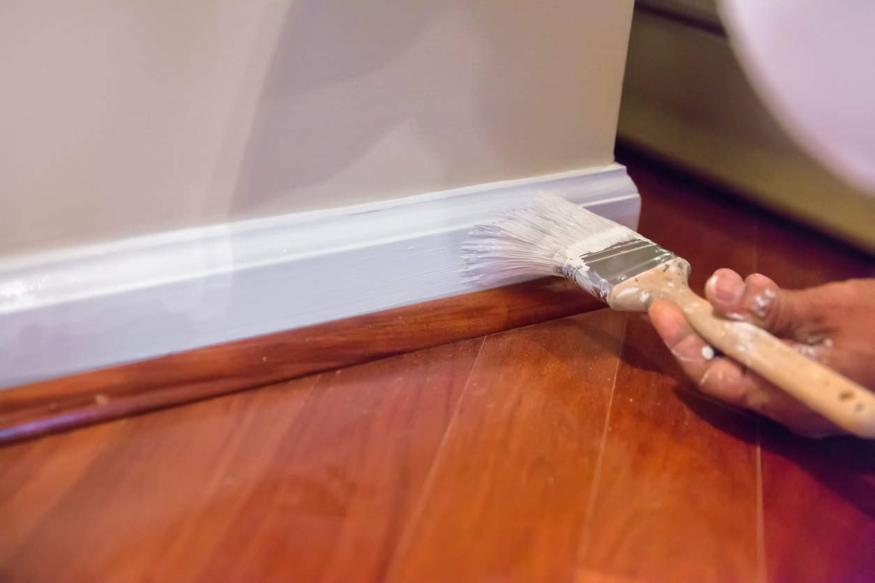 Painting white baseboards above cherry wood flooring.