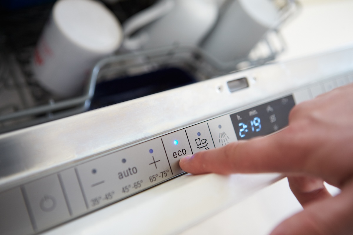 A person turning on the eco setting for their dishwasher.