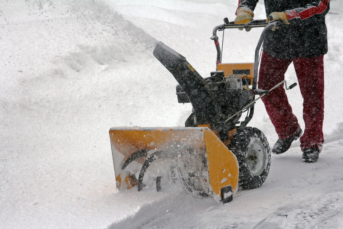 Man in snow gear using yellow snowblower during snow storm.