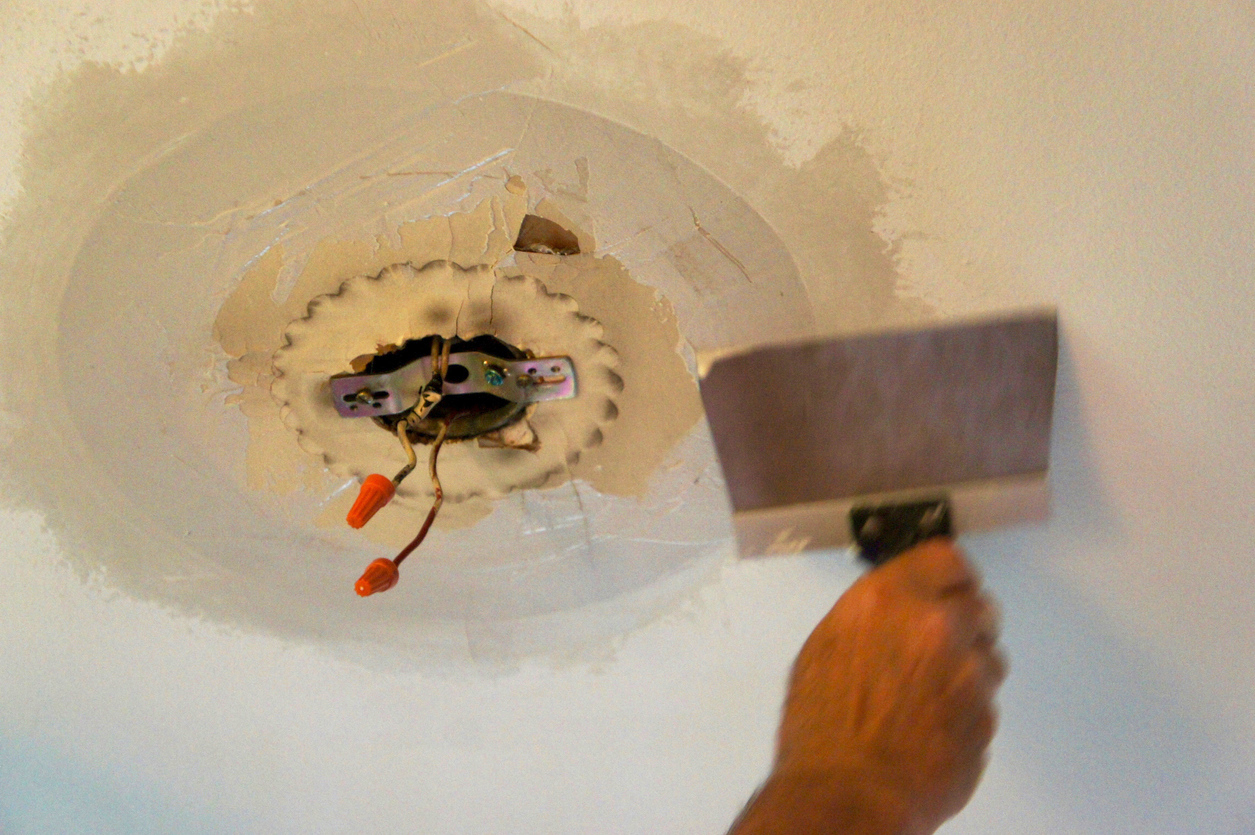 A-hand-uses-a-putty-knife-to-patch-a-ceiling-around.a-light-fixture.