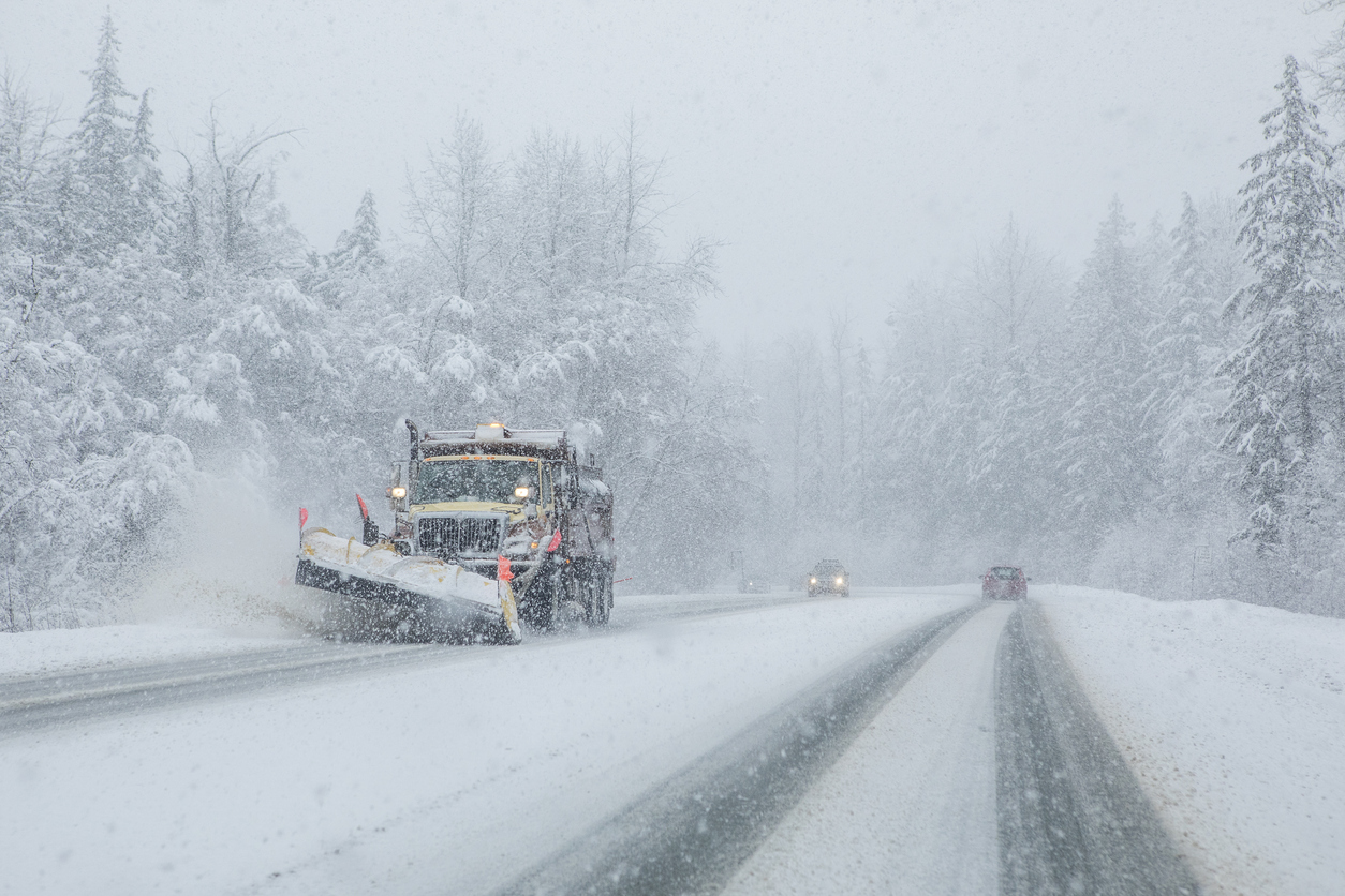 Plow truck on snowy roads with low visibility.