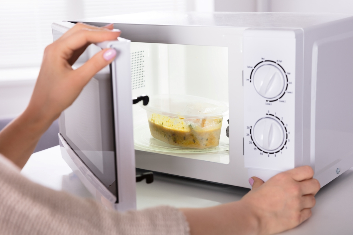 Person with plastic bowl of soup in microwave.