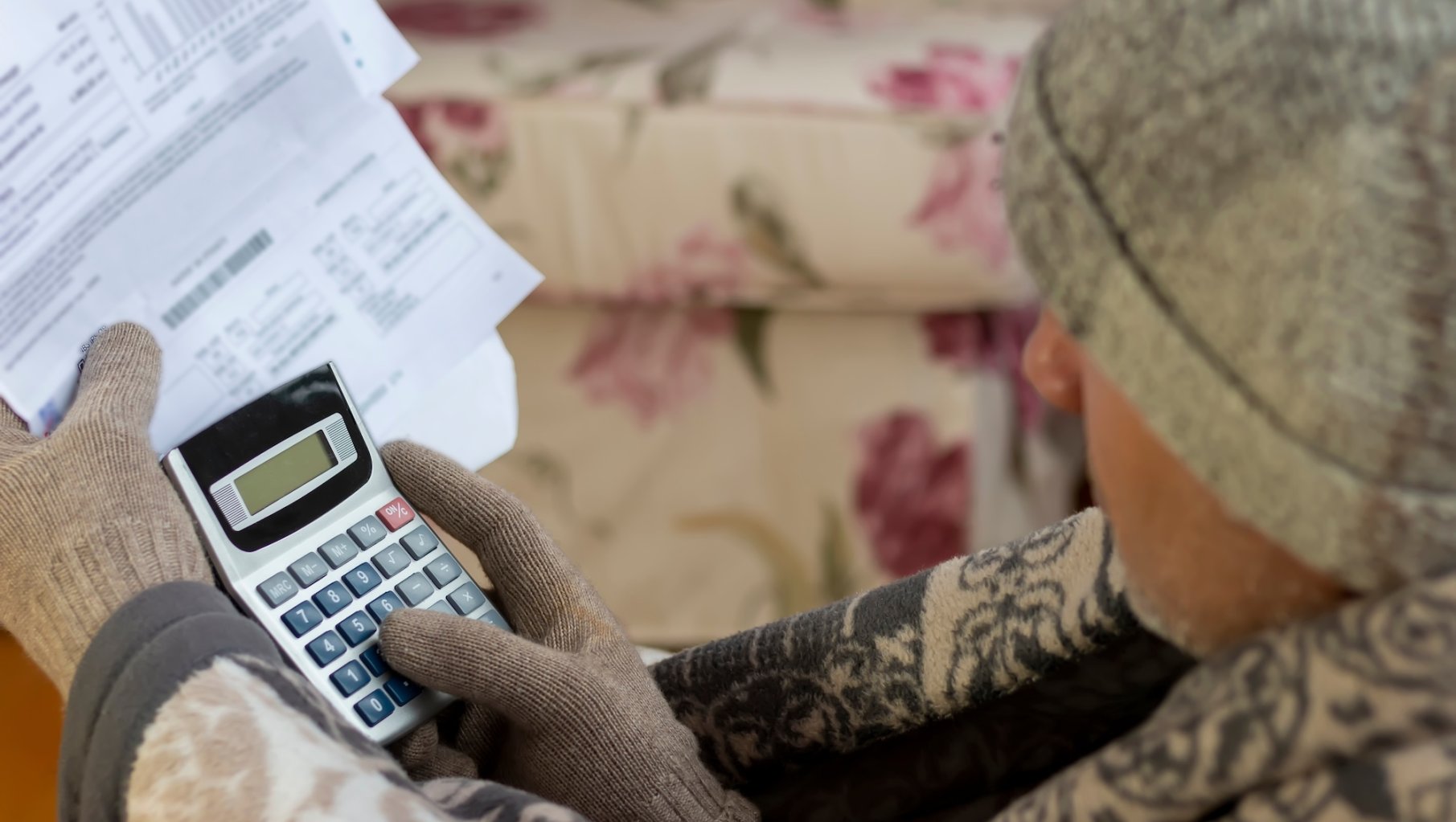 Worried mature man wearing a beanie cap reading heating bill.