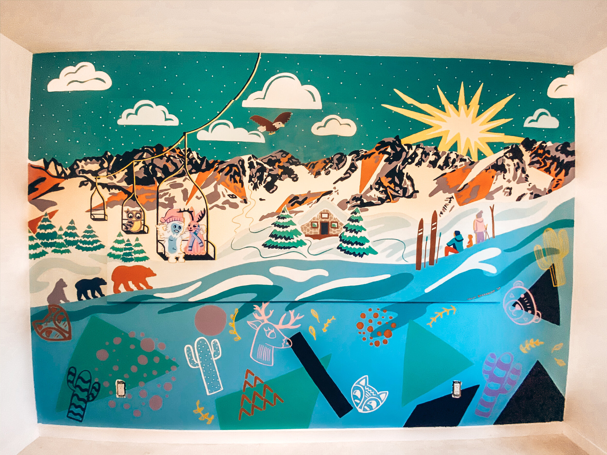 A-mural-depicting-snowy-mountains-and-a-ski-lift-in-bold-shapes-and-colors-is-painted-a masonite-board-attached-on-a-wall.