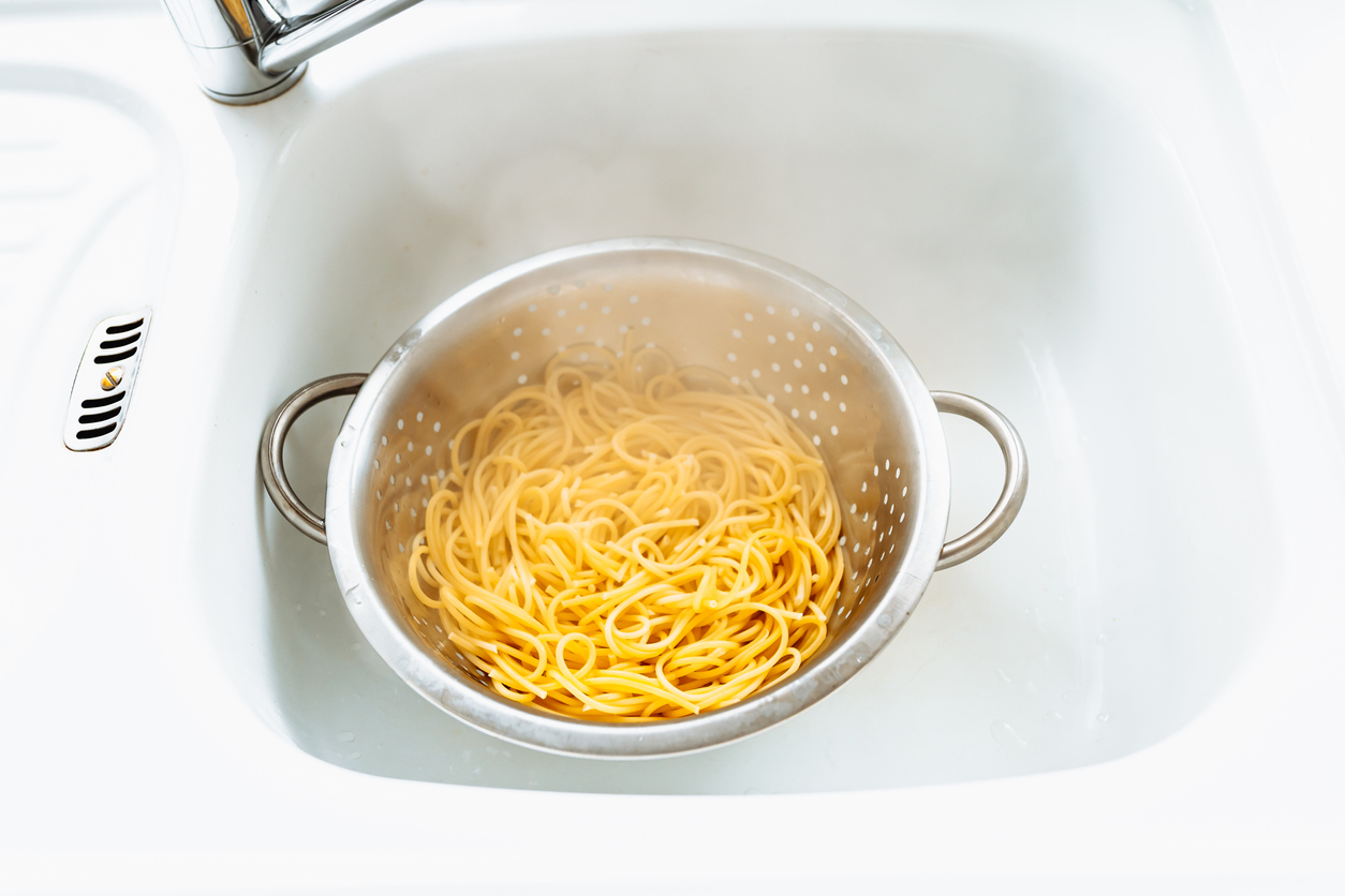 Boild spaghetti in a white colander, inside a white kitchen sink.