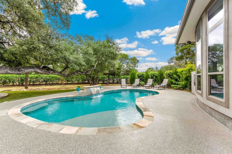 Kidney-shaped swimming pool in the back of a luxury home.
