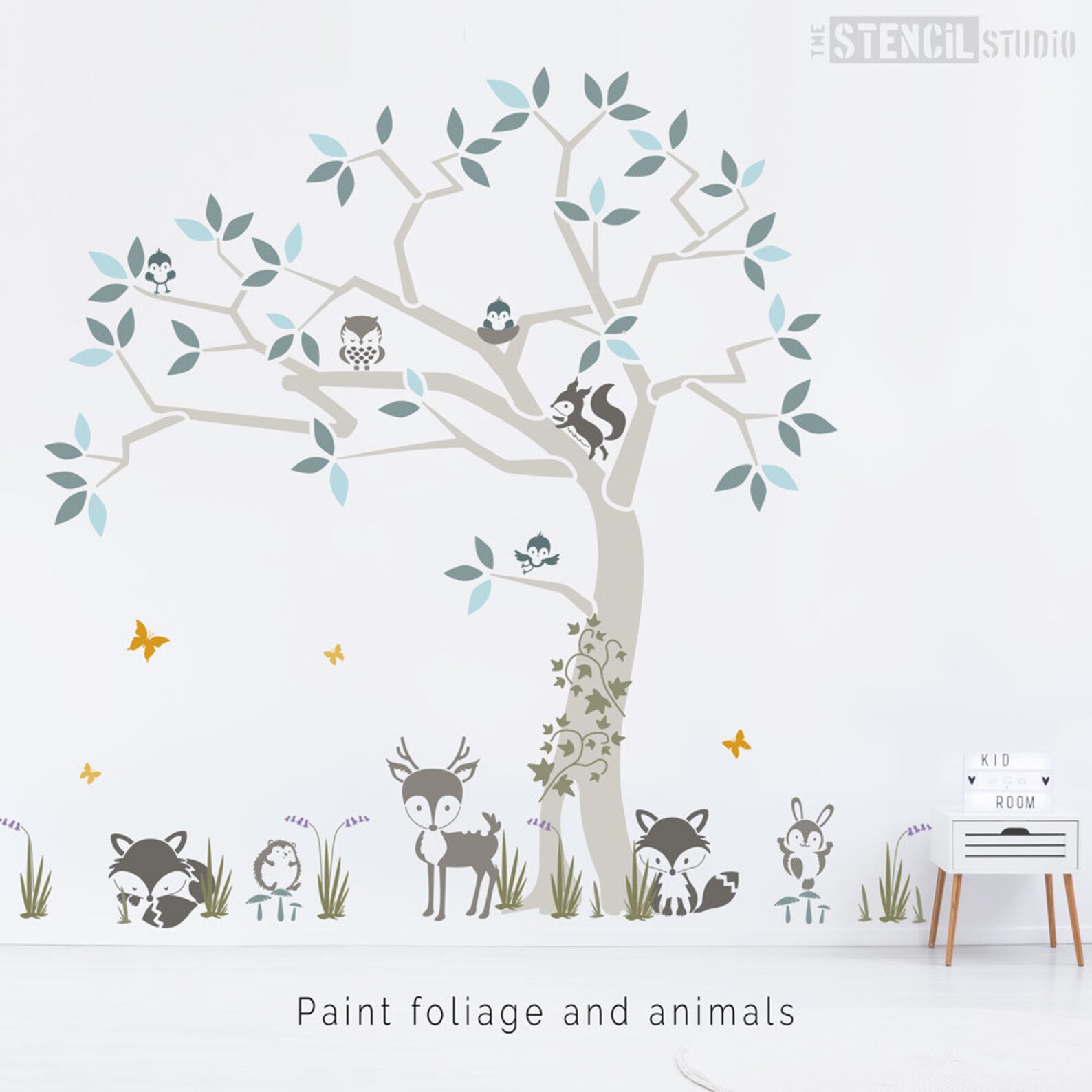 A wall is painted with a woodland tree scene with animals in grey and pastel colors.