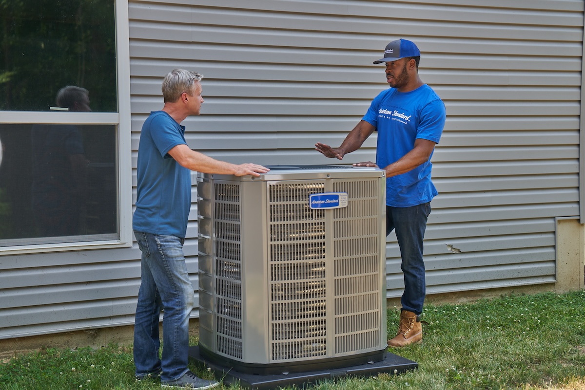 American Standard HVAC professional speaking to a homeowner about the heat pump being installed outside a home.