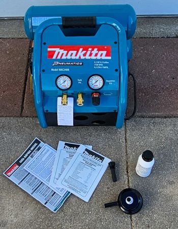 The Makita MAC2400 2.5 HP Air Compressor with its instruction manual and included extras on a cement surface before testing.