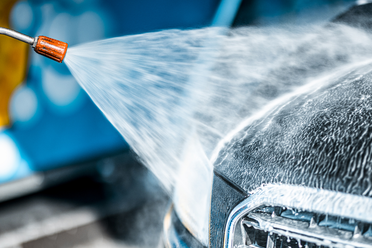 A wide spray of water from the best pressure washers for cars hitting a soapy car to rinse it clean.