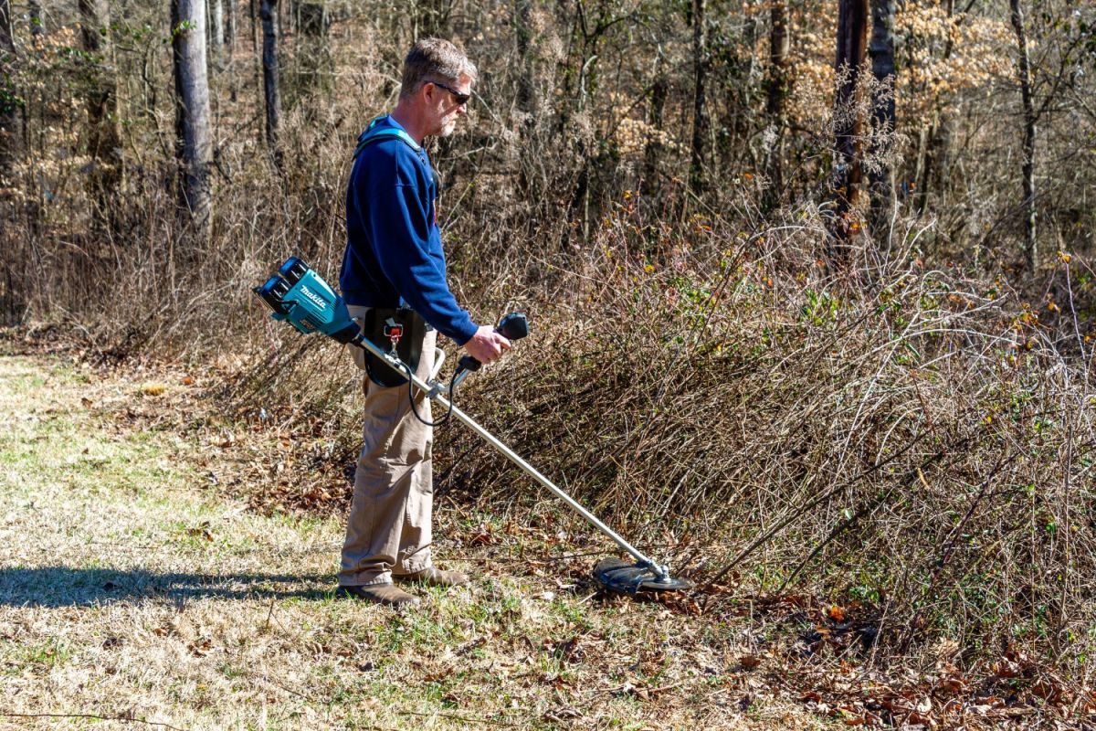 A person using the Makita brush cutter to clear vegetation along a wooded area.