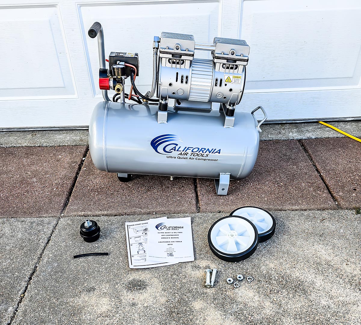 The California Air Tools 8010 Ultra Quiet Air Compressor on a cement pad with all its included manuals and accessories.