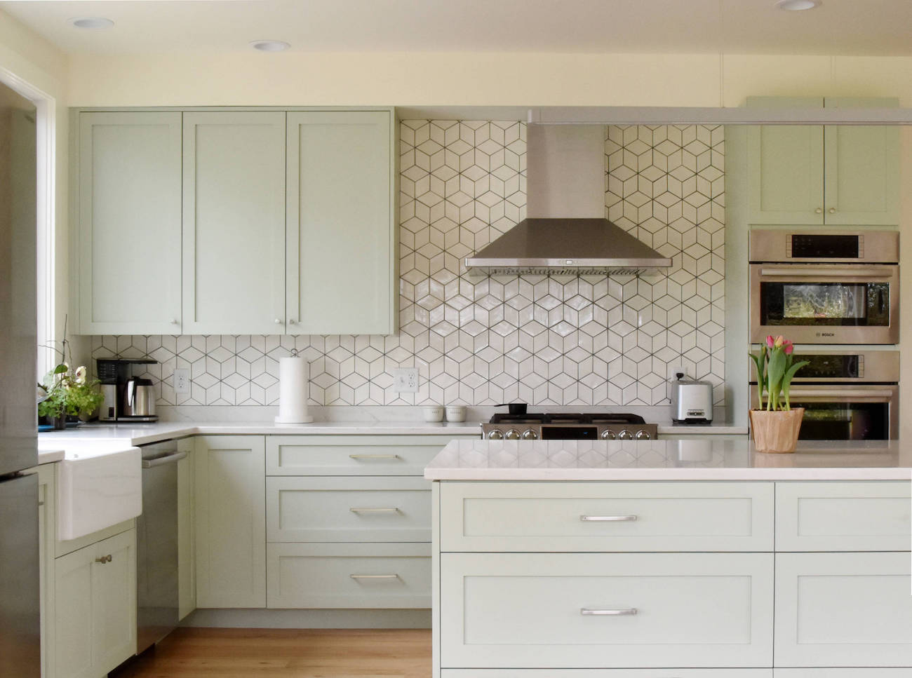 A pale green kitchen has a dual fuel range with gas stovetop.