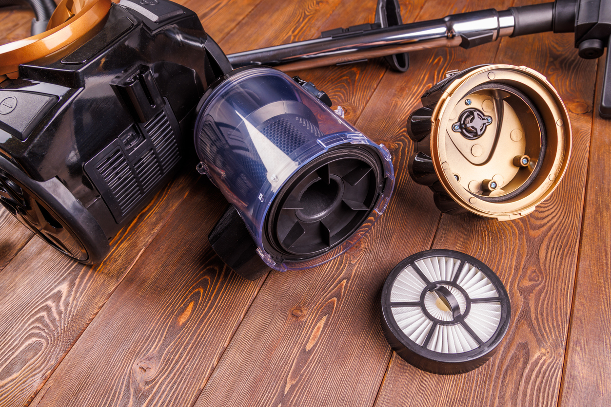 A disassembled vacuum cleaner sitting in pieces on a hardwood floor.