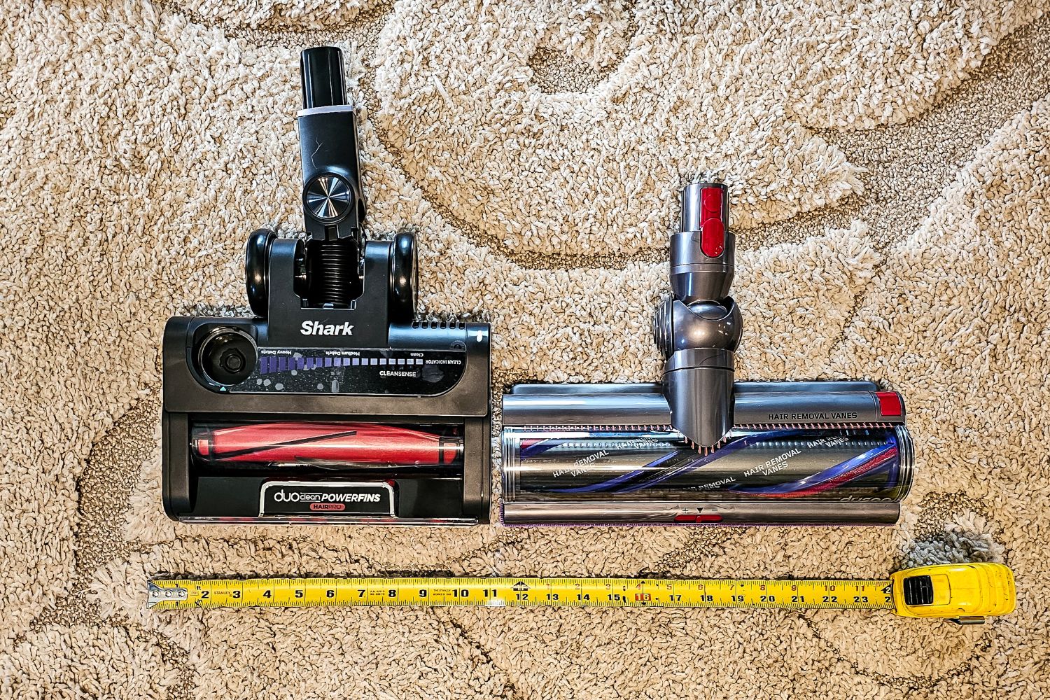 The cleaning heads of Dyson vs Shark on a rug next to a measuring tape showing the Dyson head is wider.