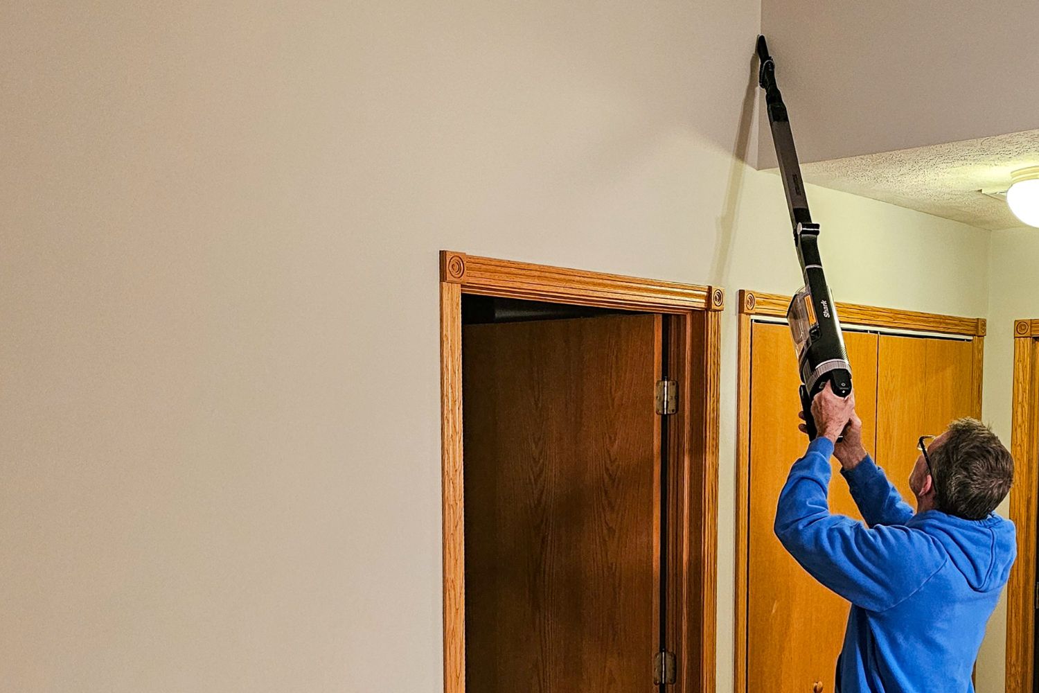 A person using the dusting attachment on the Shark Stratos cordless vacuum to clean a corner of the ceiling.