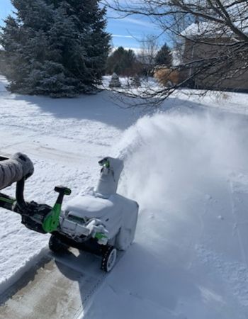 Someone using the Ego lightweight snow blower to blow snow off a sidewalk.