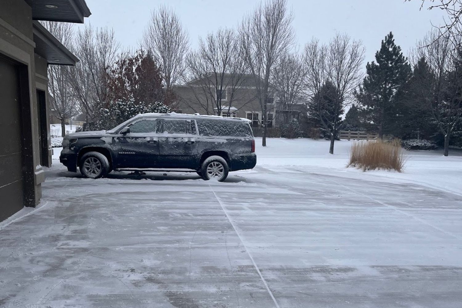 A snow-covered SUV parked at the far end of a driveway that has been mostly cleared using the Ego lightweight snow blower.