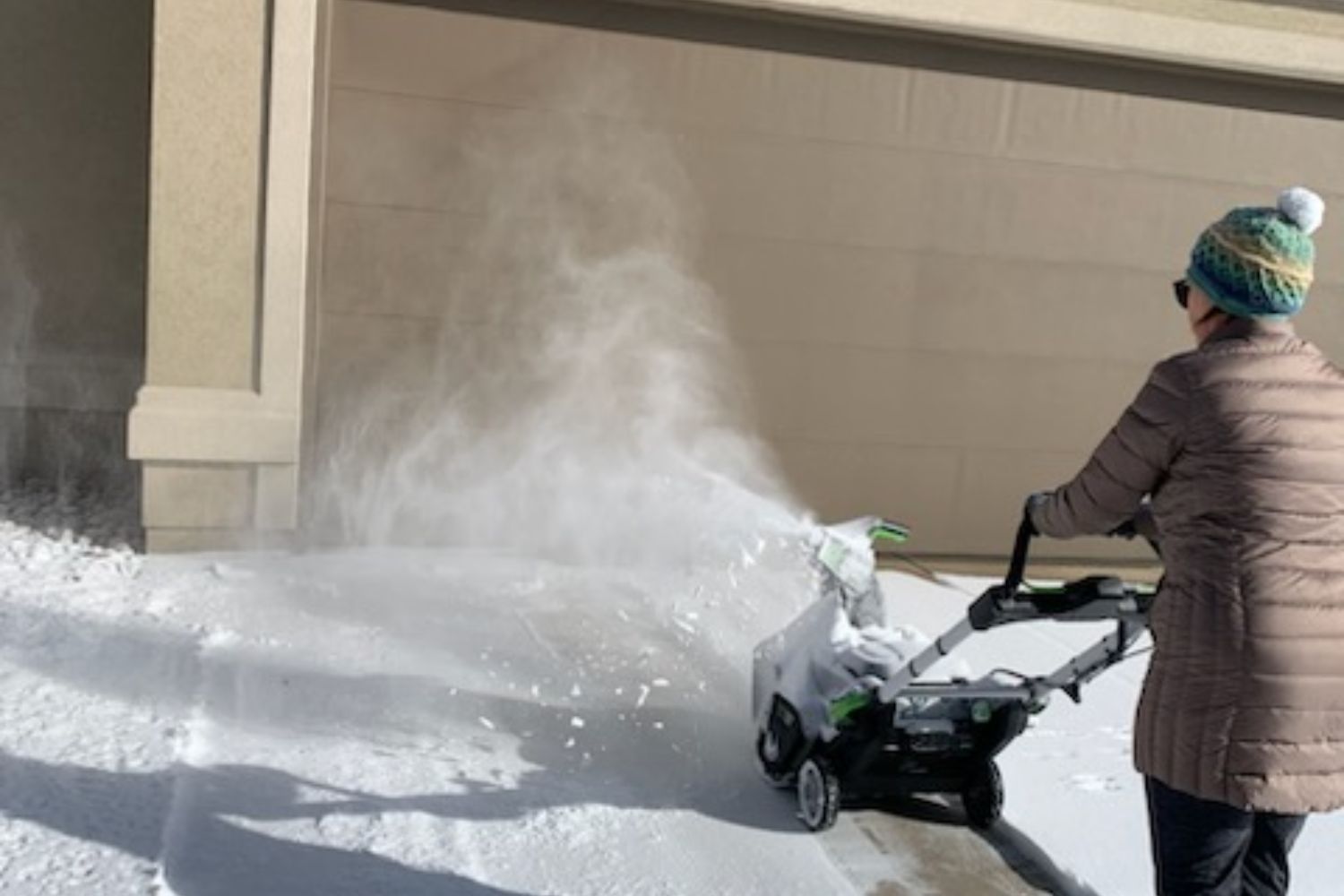 Someone using the Ego lightweight snow blower to blow snow off a driveway.