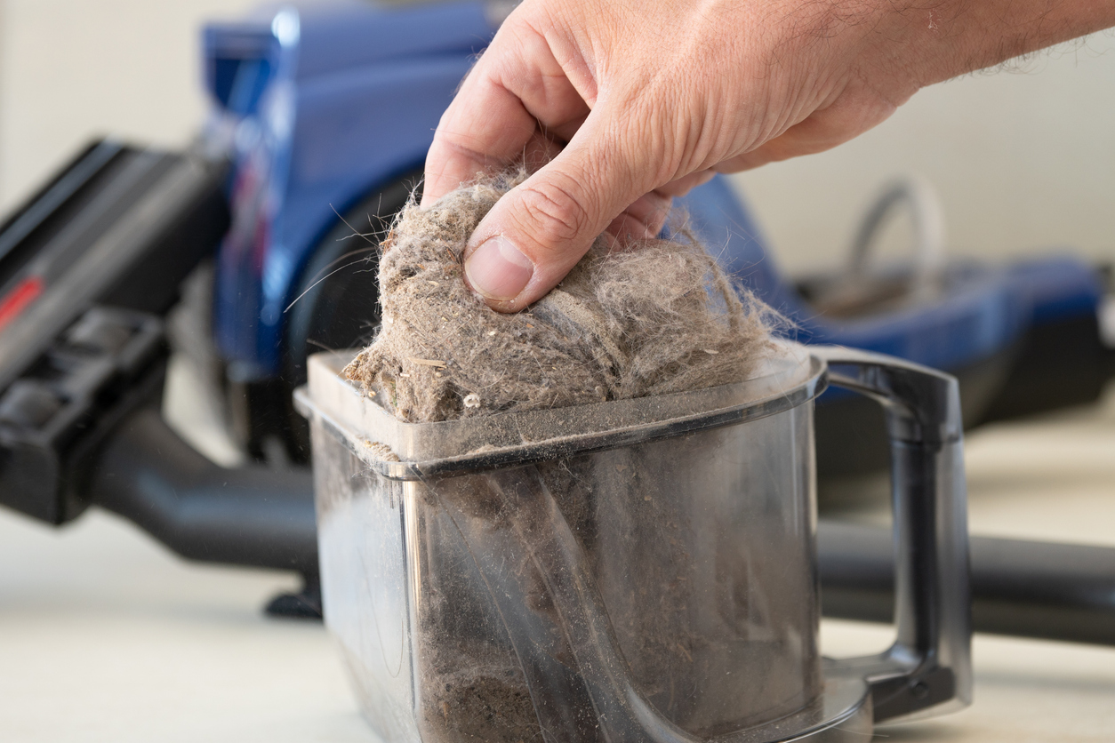 A man pulling a large clump of dust and hair from a removed vacuum dust compartment.