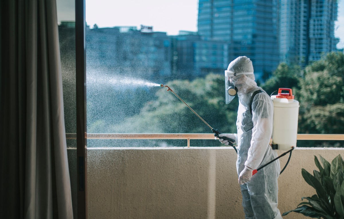 A view of a person in a hazmat suit spraying a pest control solution from a balcony. 