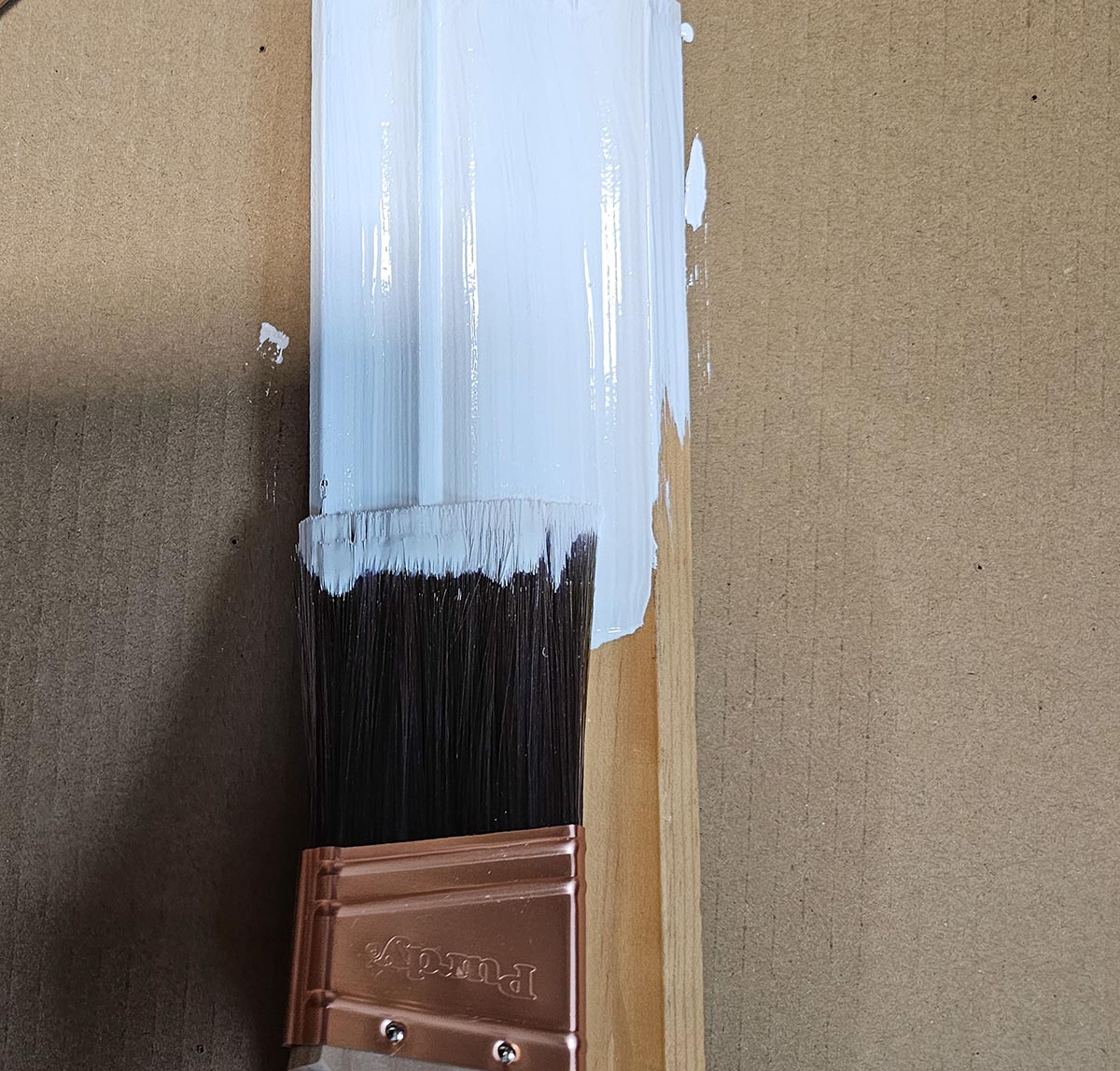 The Purdy 2-inch XL Glide Paint Brush in use for painting a piece of wood trim white.