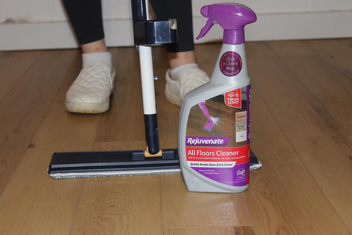 A spray bottle of the Rejuvenate All Floors Cleaner next to a mop during testing to clean a wood floor.