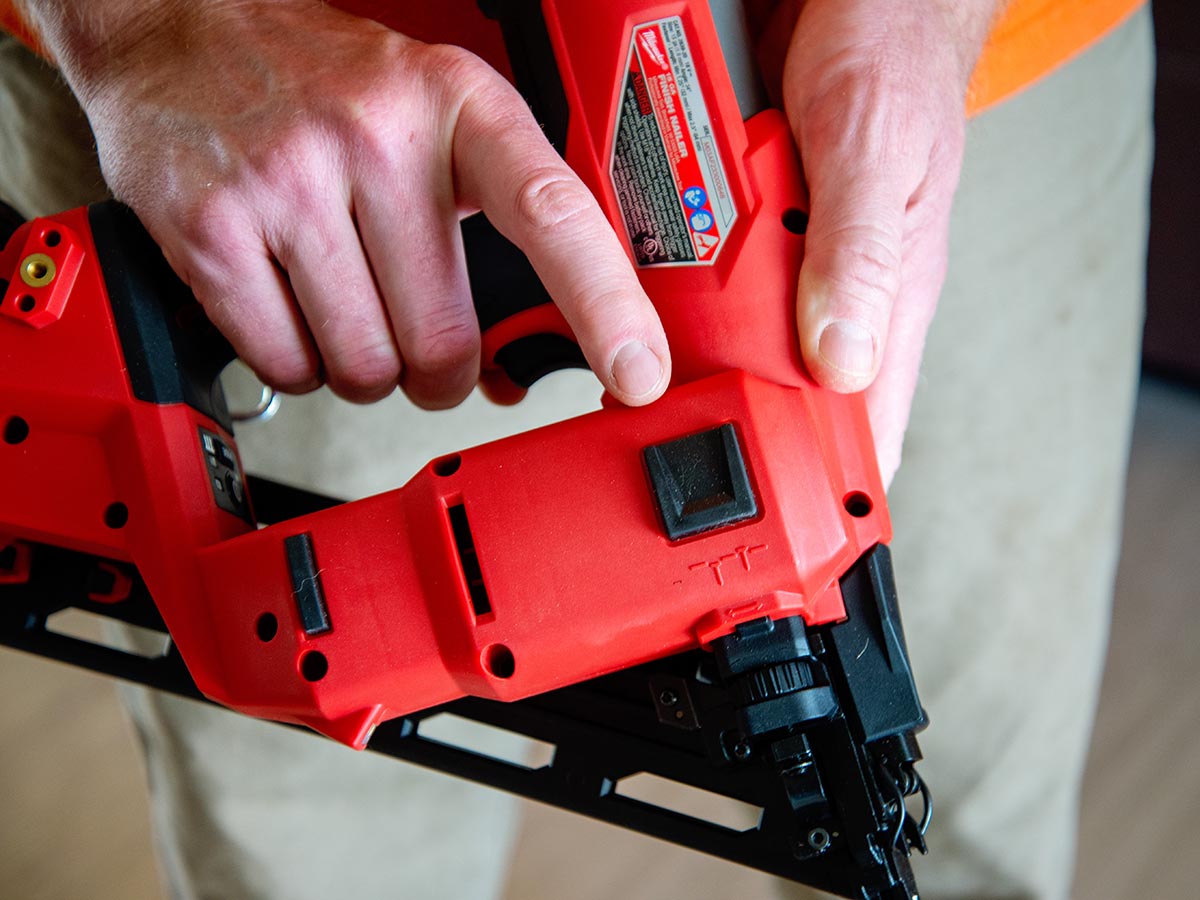 A person's finger next to the sequential and contact actuation modes switch on the Milwaukee 15-Gauge Finish Nailer.