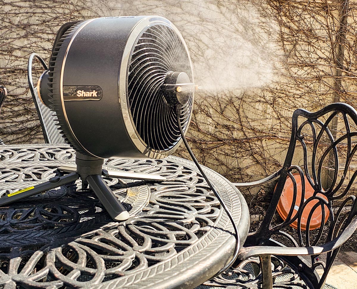 The Shark FlexBreeze Fan with InstaCool set up on. patio table during testing and blowing a cool mist into the air.