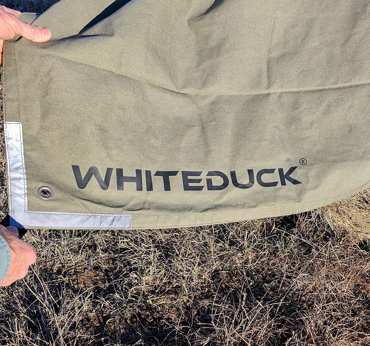 A person holding the corner of the White Duck tarp review out to show it's reinforced grommet and corner.