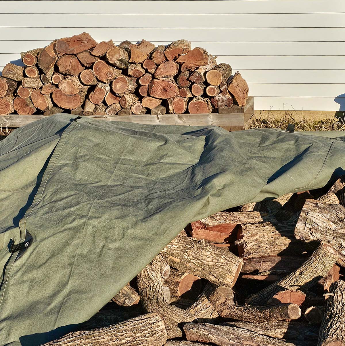 The White Duck Tarp partially covering a stack of firewood with one corner folded back.