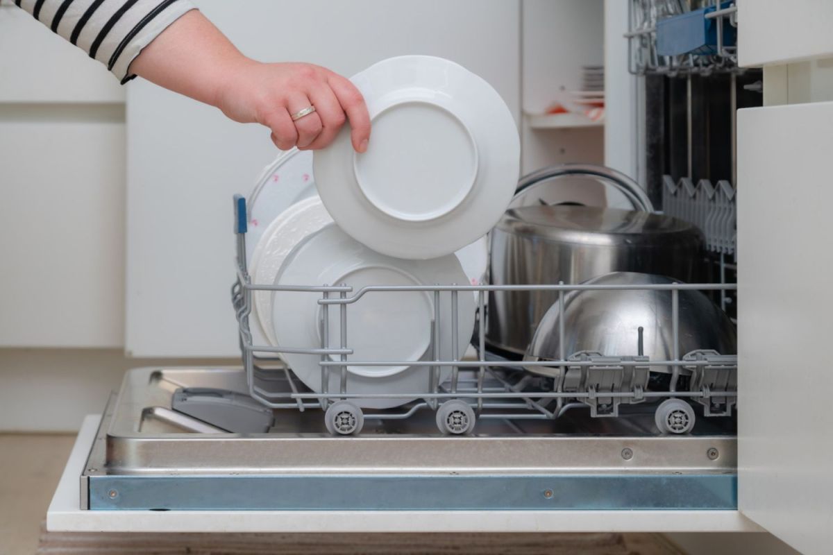 A person putting a plate into a drawer dishwasher.