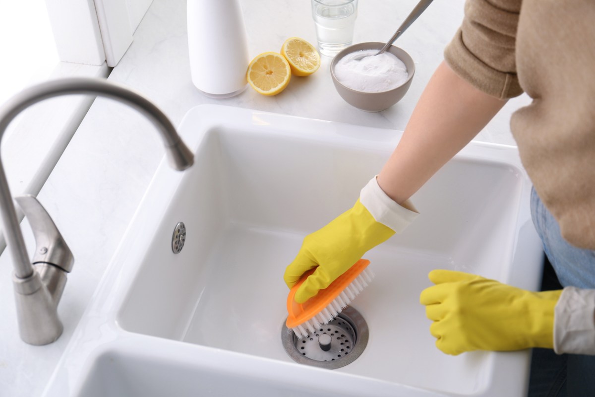 Woman using baking soda and brush to clean sink, with lemons on the counter next to her.