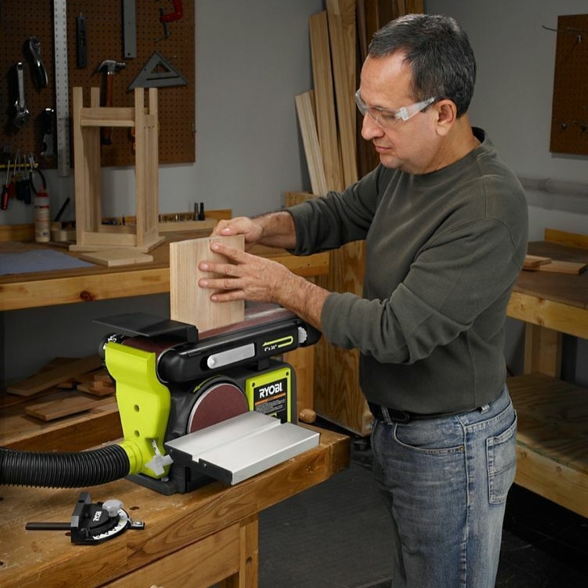 Man with goggles sanding wood with large green table sander.
