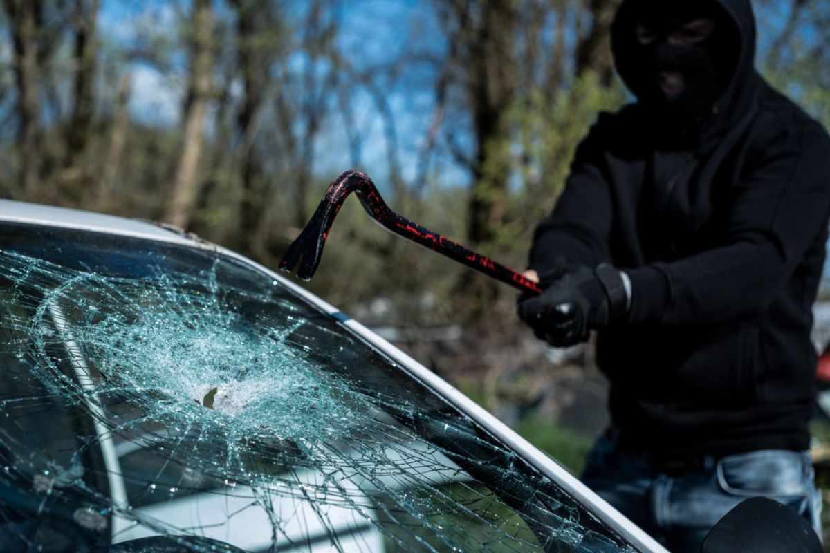 A burglar breaks the glass of a car.