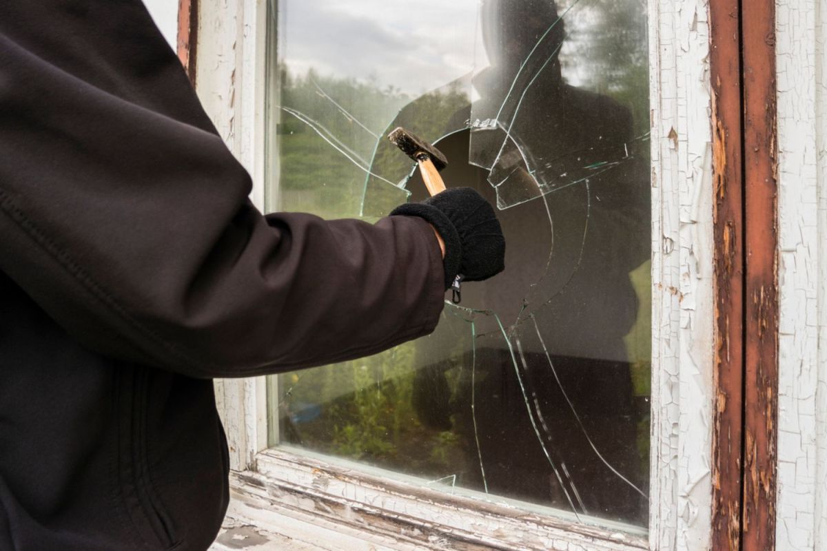 A burglar dressed in black breaks a window.