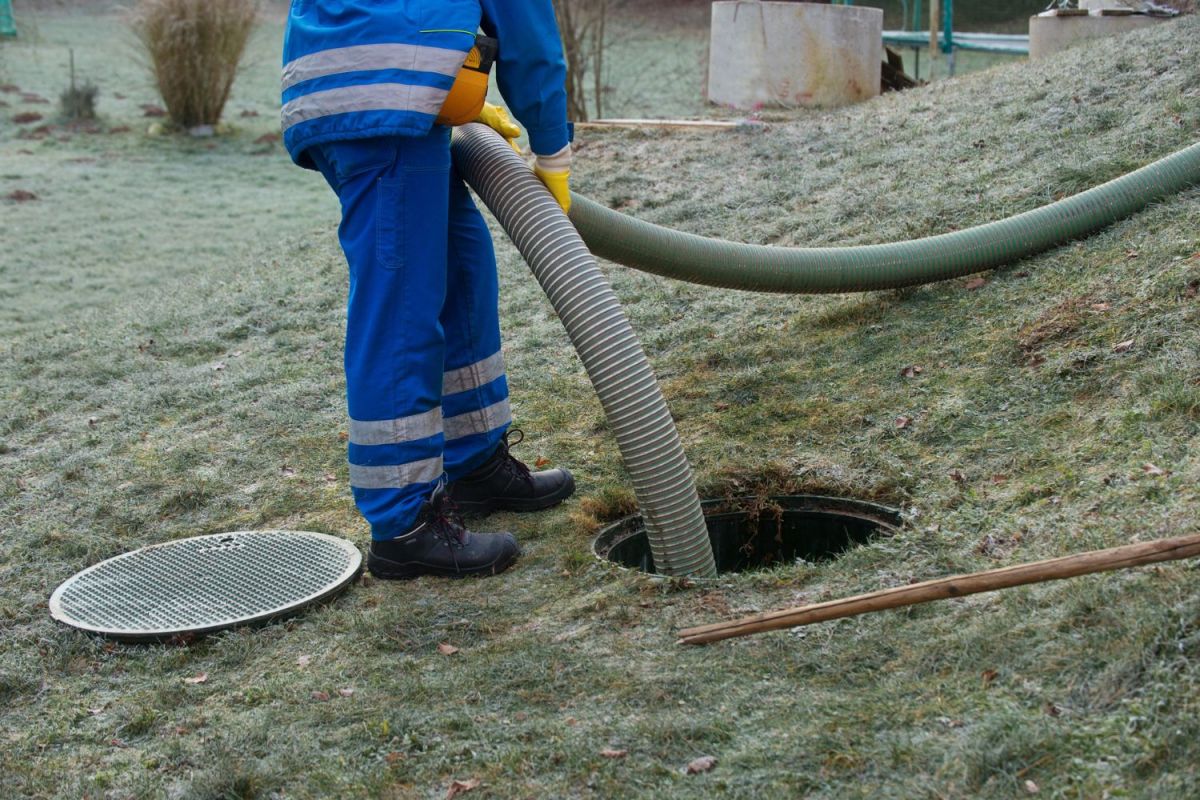 A worker lowers a hose in a pipeline in a yard. 