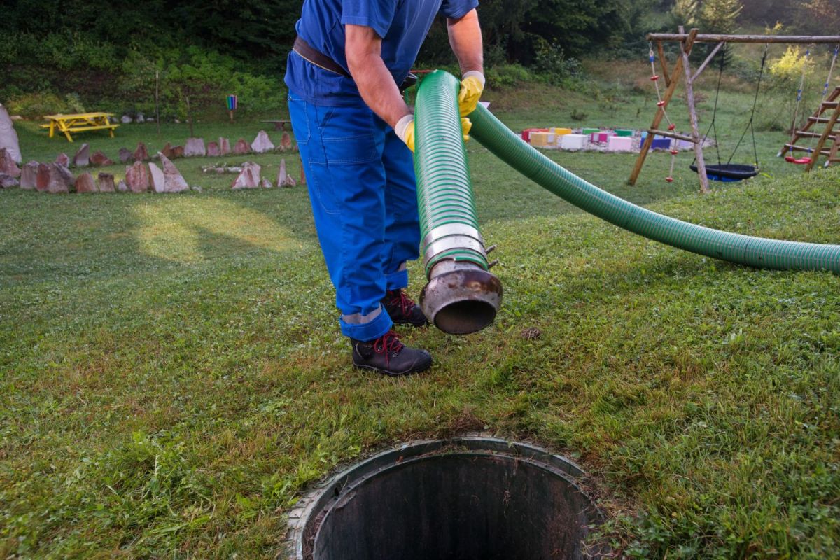 A close up of a worker putting a large hose into a pipe in a lawn.