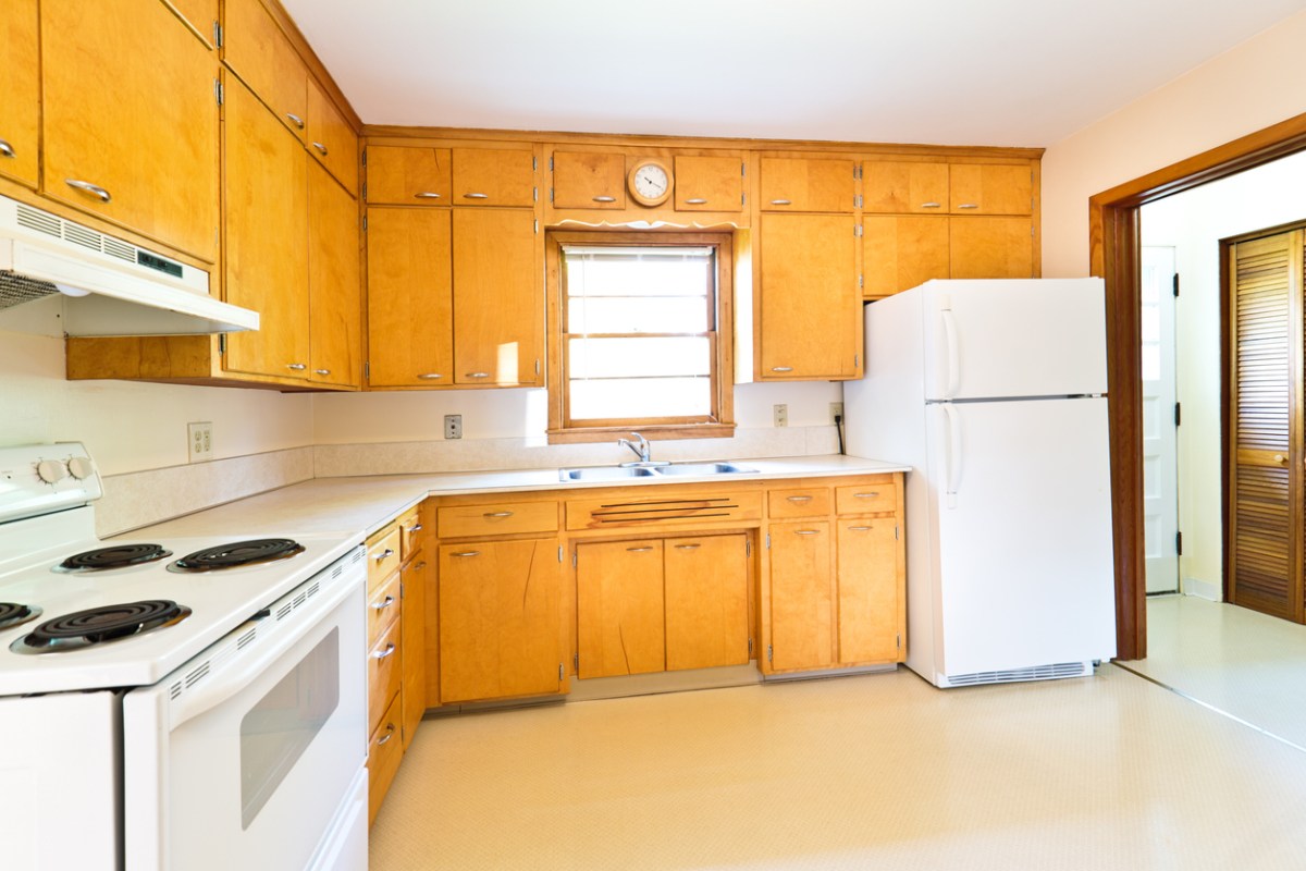 An-outdated-kitchen-with-oak-cabinets-and-white-appliances-spread-too-far-apart.