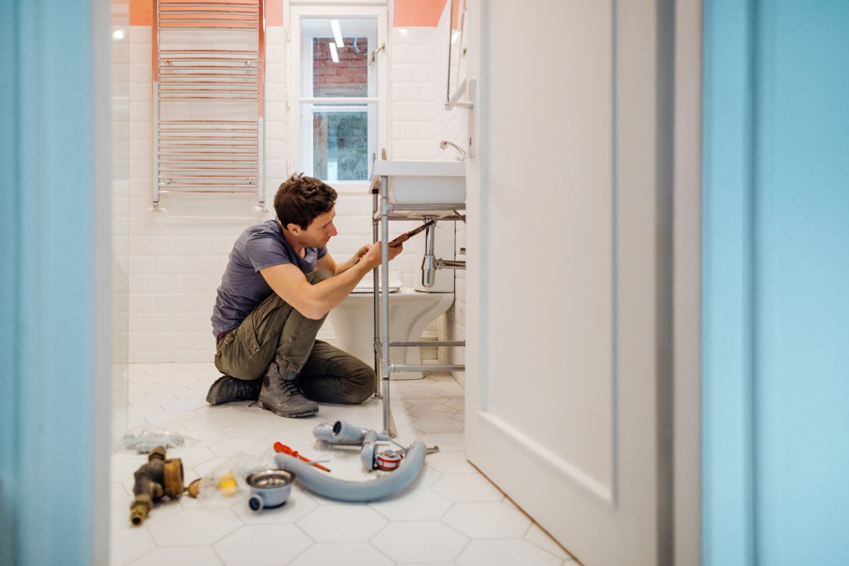 Young man fixes plumbing under a bathroom sink.