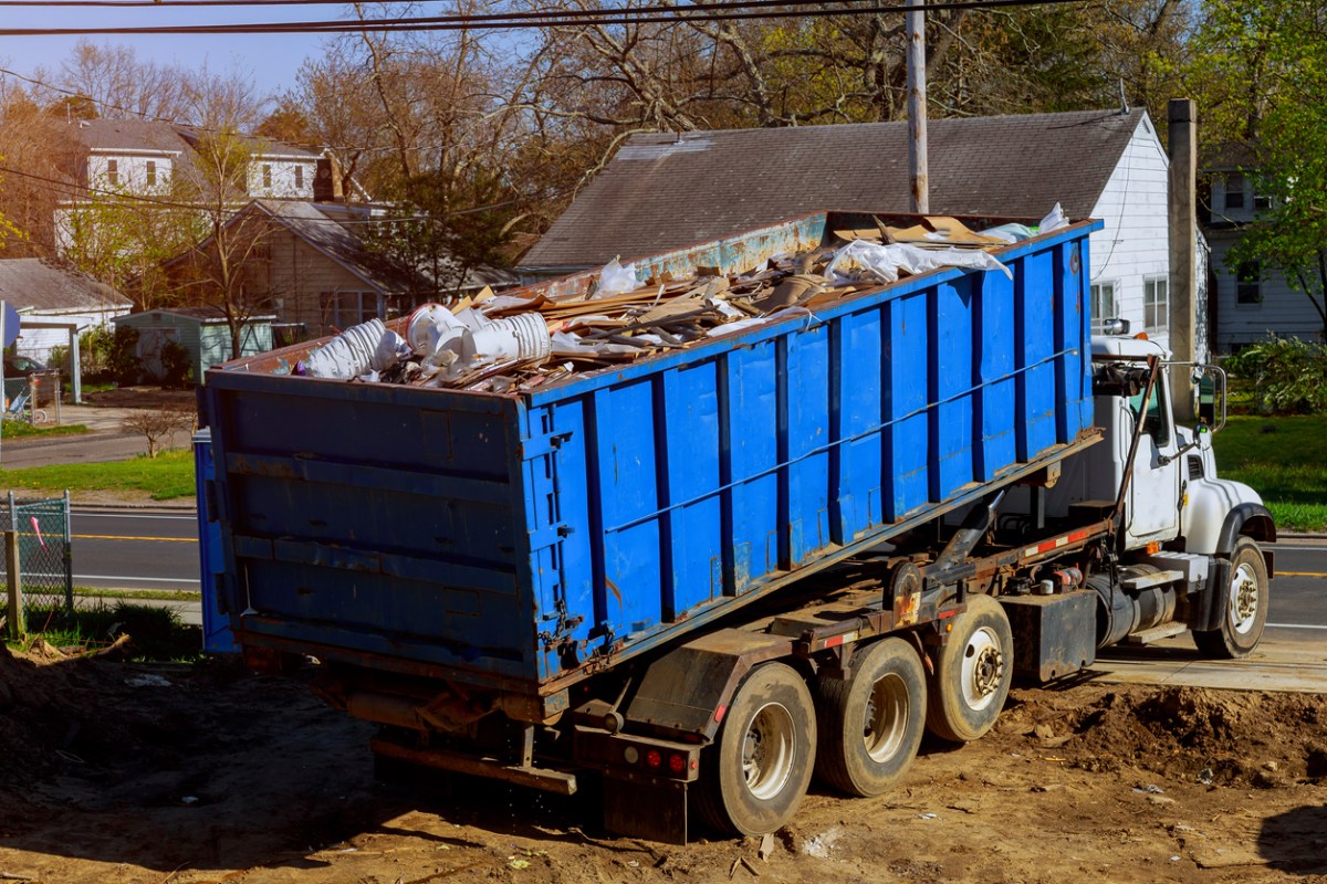 Blue junk container gets hauled away by white truck.