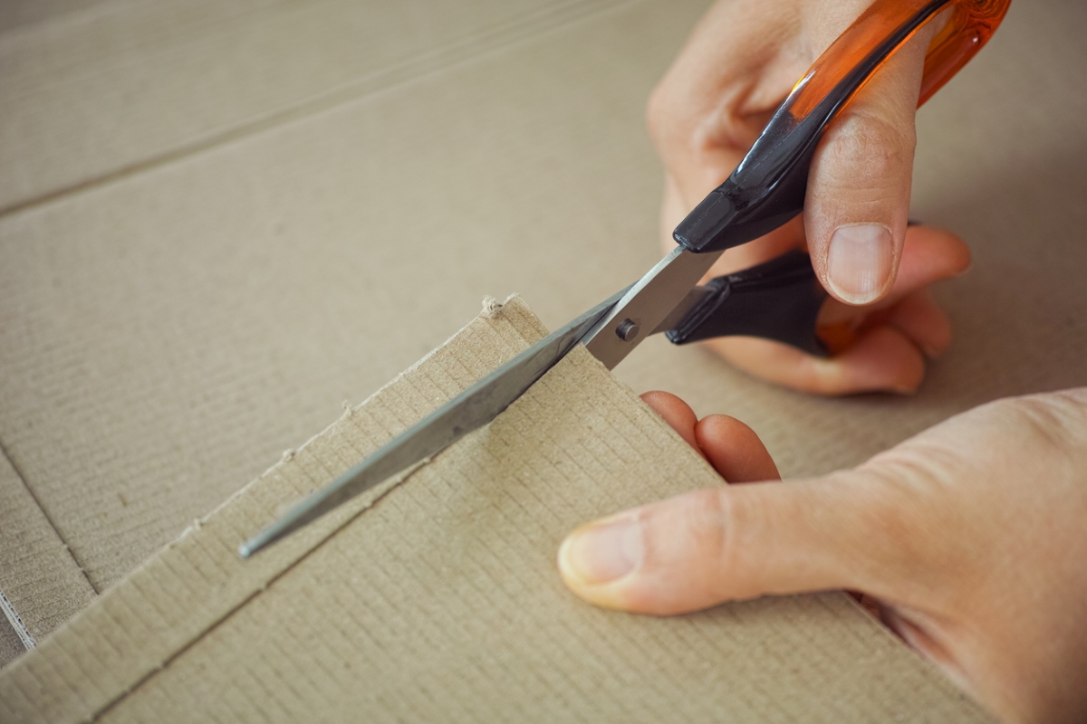 Hands using scissors to cut cardboard.
