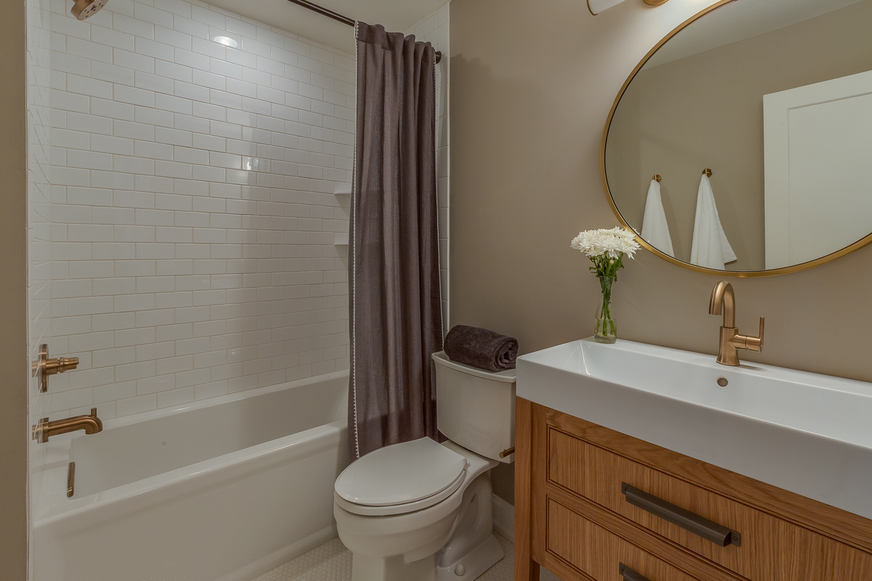 Full bathroom with white combined shower and tub with circular gold mirror.